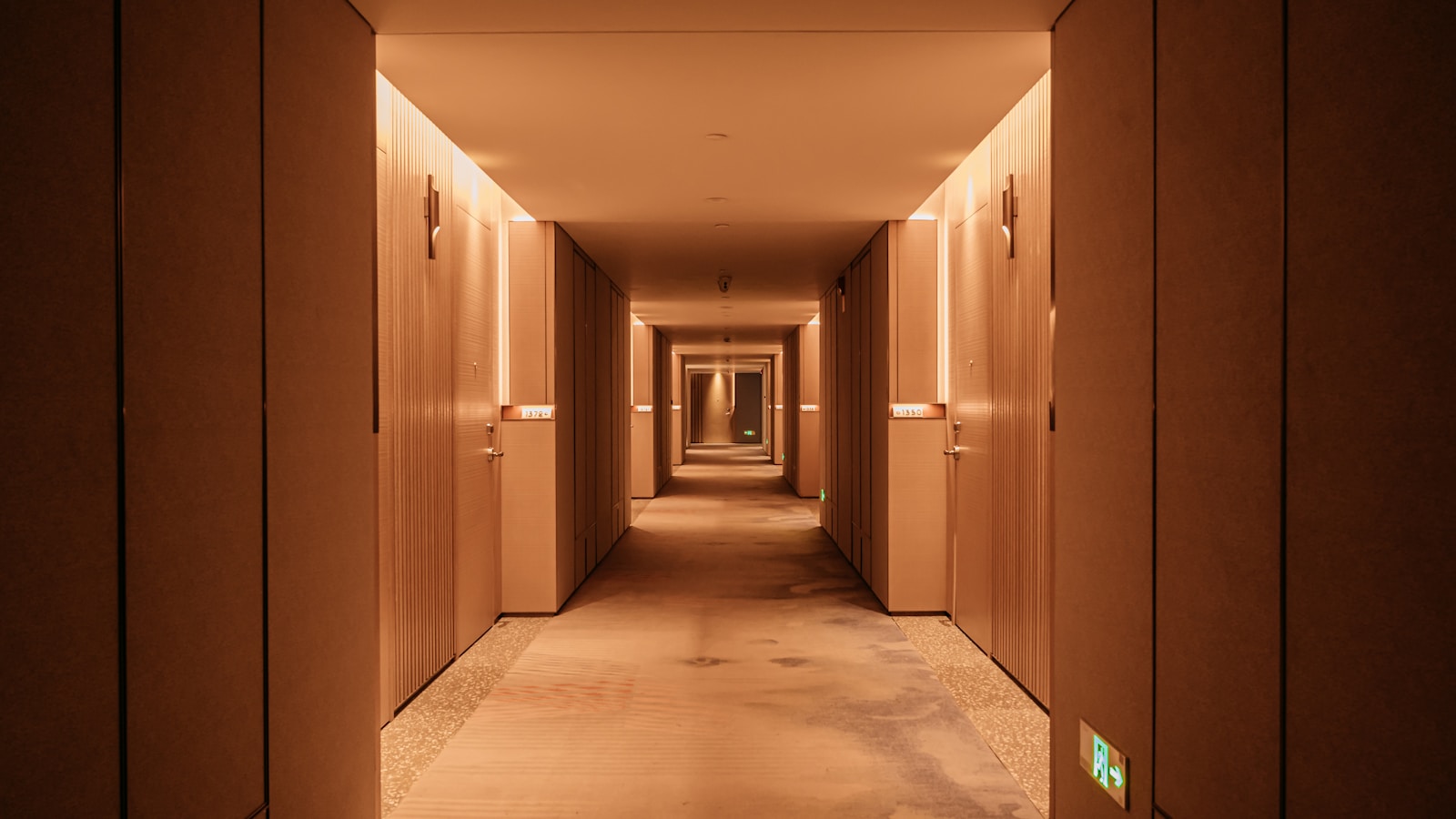 Couloir d'hôtel avec plaques de numéros de chambre et plan d'évacuation au mur